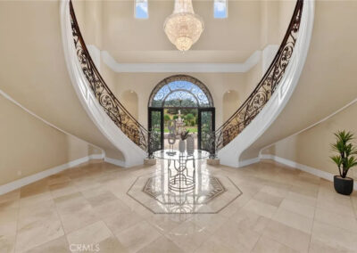 Grand curved symetrical freestanding staircase with custom wrought iron railing, marble floors, and chandelier in luxury home interior