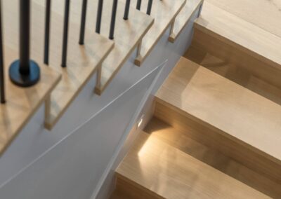 White oak modern staircase detail with 1 3/16 inch wood treads, white skirting, and integrated stair lighting