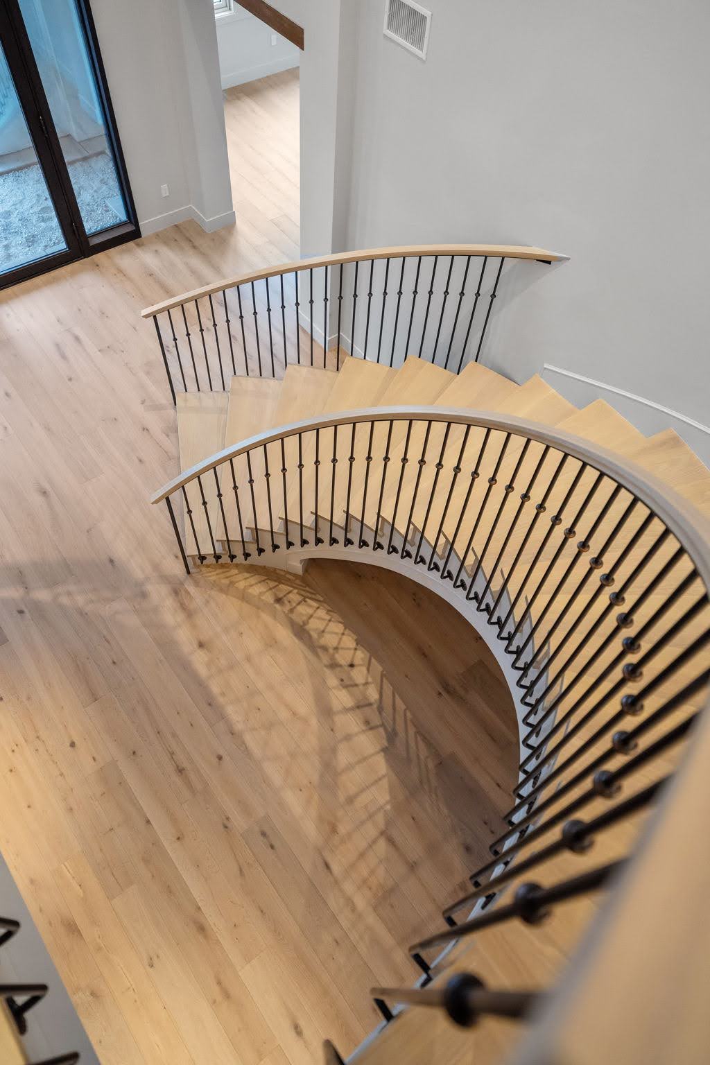 Custom curved free standing wood staircase with wrought iron railing in luxury home